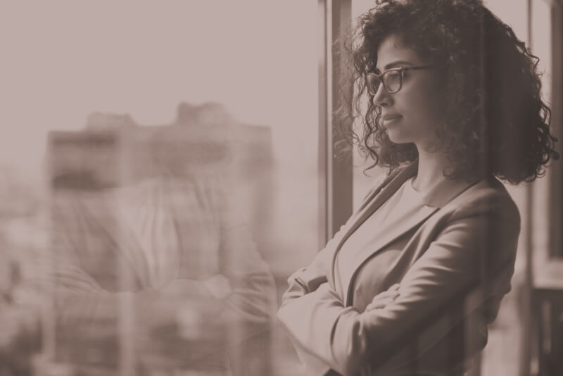 A woman stands and gazes out an office window.