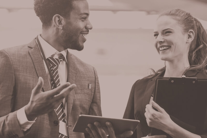 A man and a woman speak to one another. They are smiling.