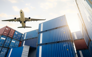 Airplane flying over shipping containers.